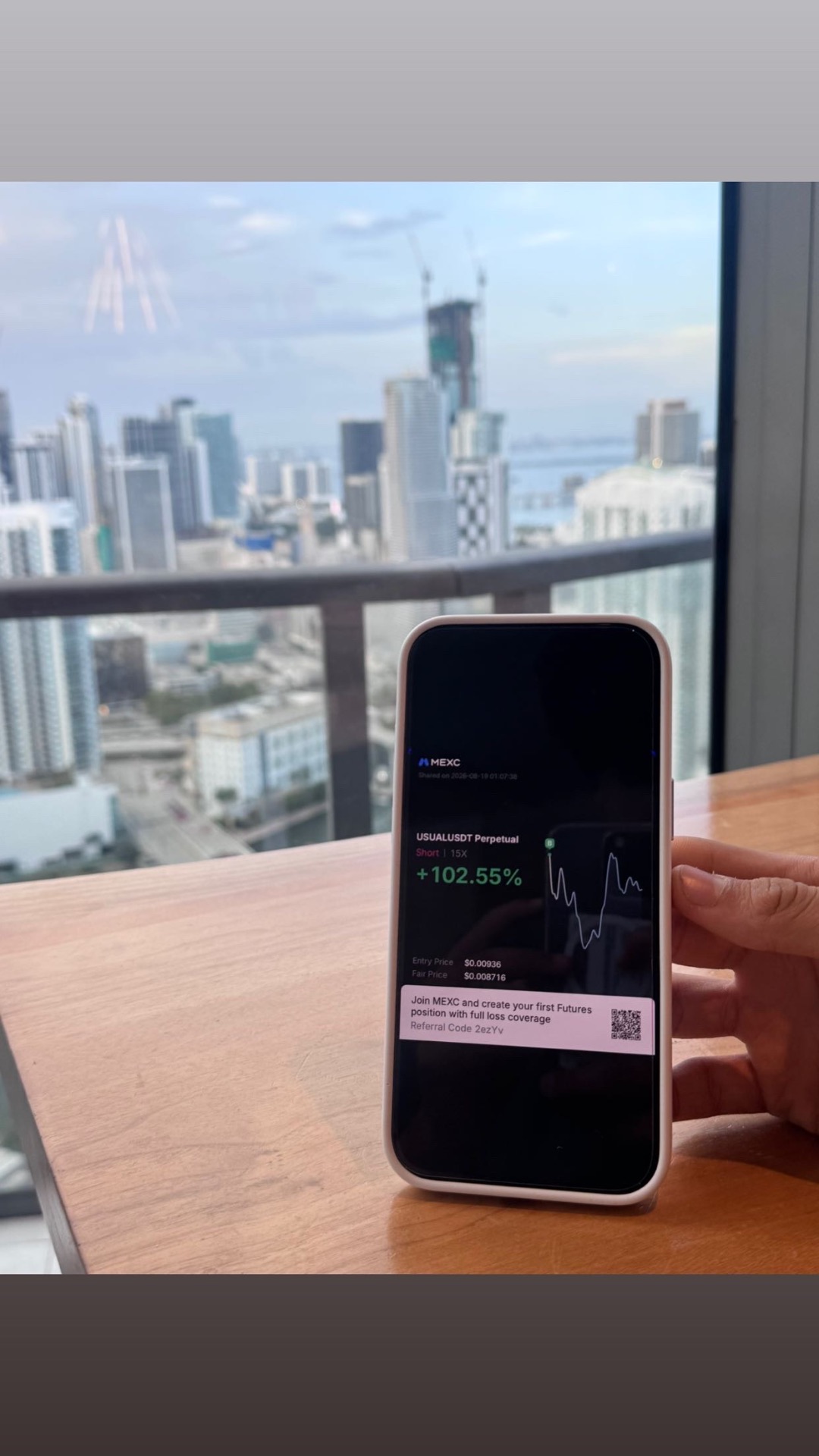 Phone showing a USUAL/USDT short position up 102.55% over a city skyline