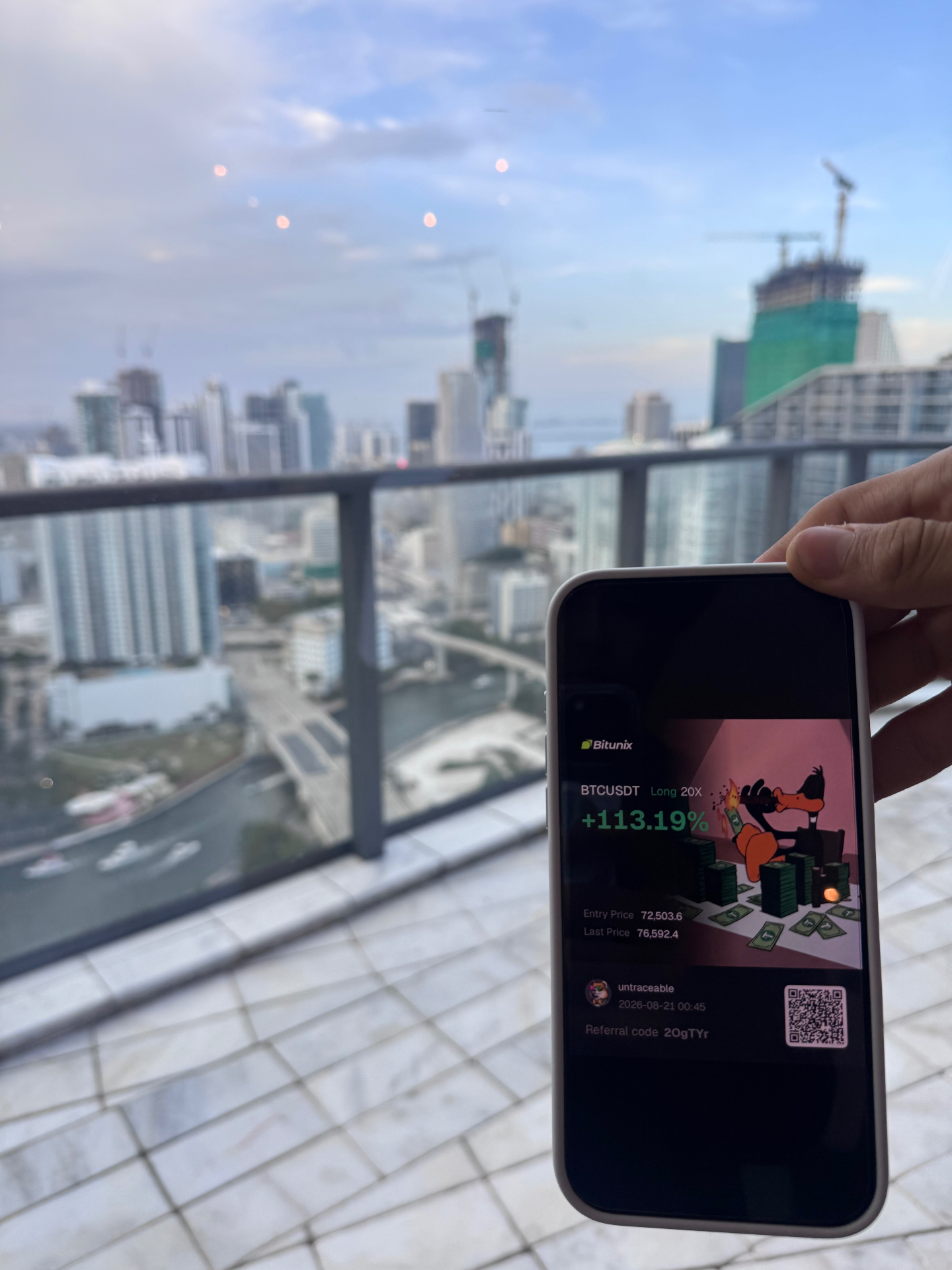 Phone showing a BTC/USDT long position up 113.19% on a balcony